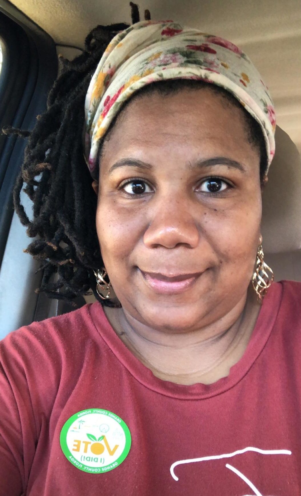 Photo of Black female teacher wearing a red shirt, sitting in a car