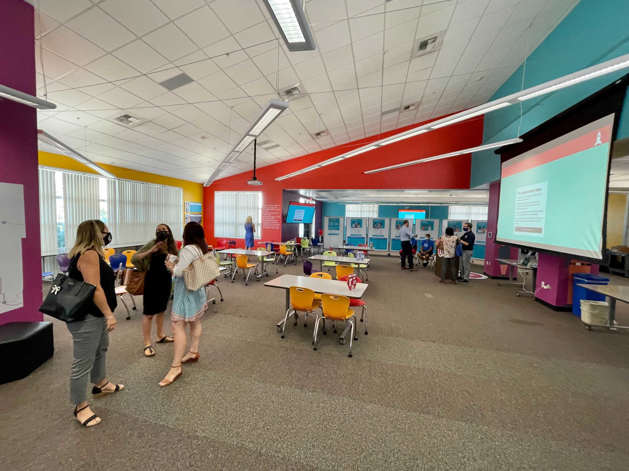 Photo of library space with multicolor walls and desks in the center, a few women with face masks are standing on the left