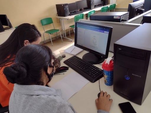 Two people sitting in front of a computer screen that is displaying a logo design.