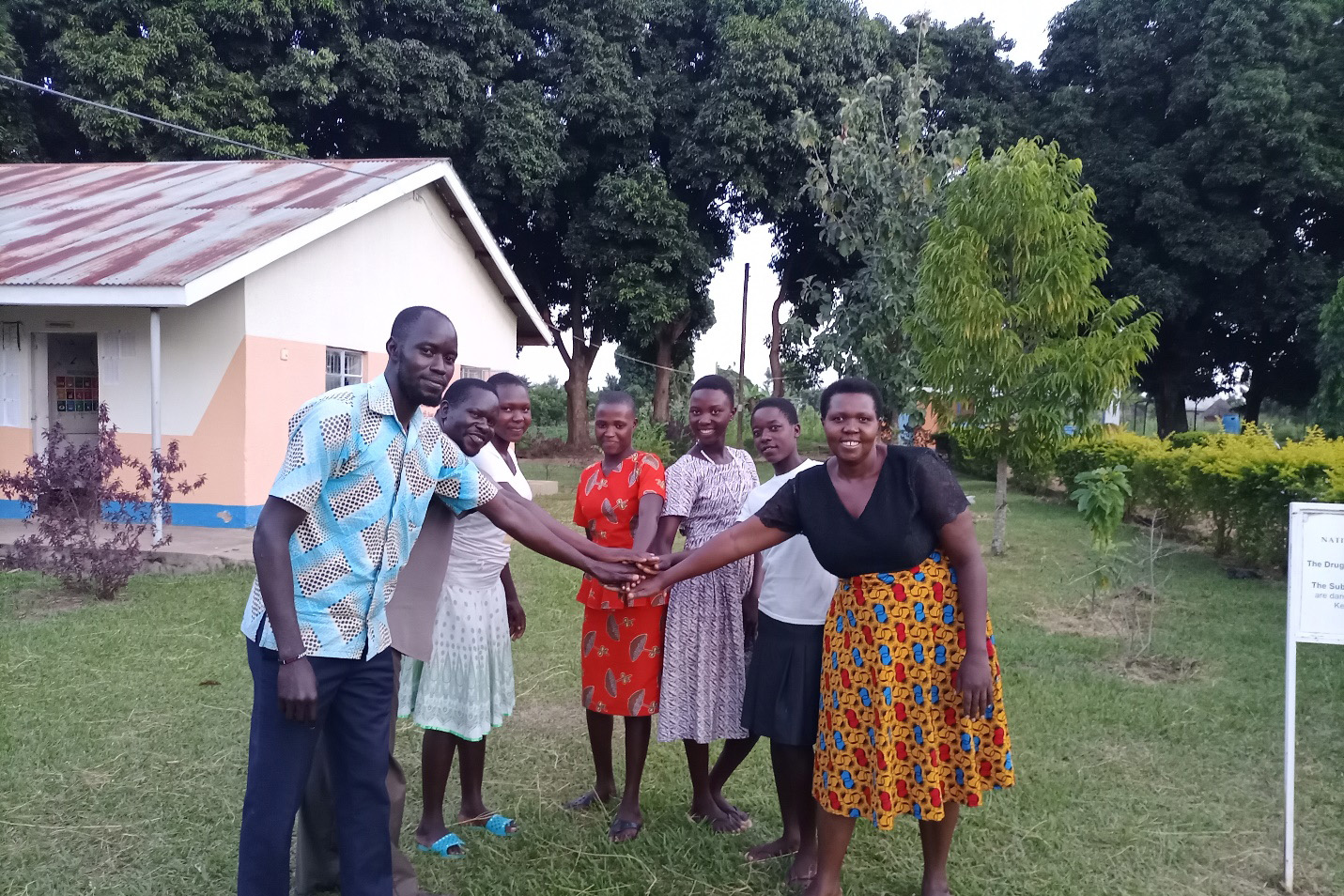 Seven people standing outside in a half circle with hands together.