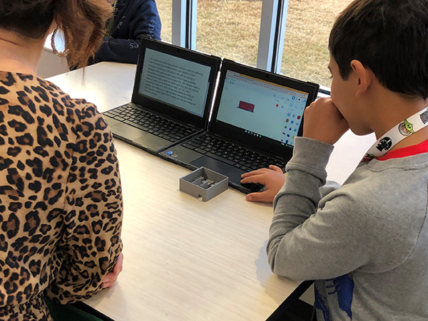 Two students looking together at two laptop screens with text and images on them.