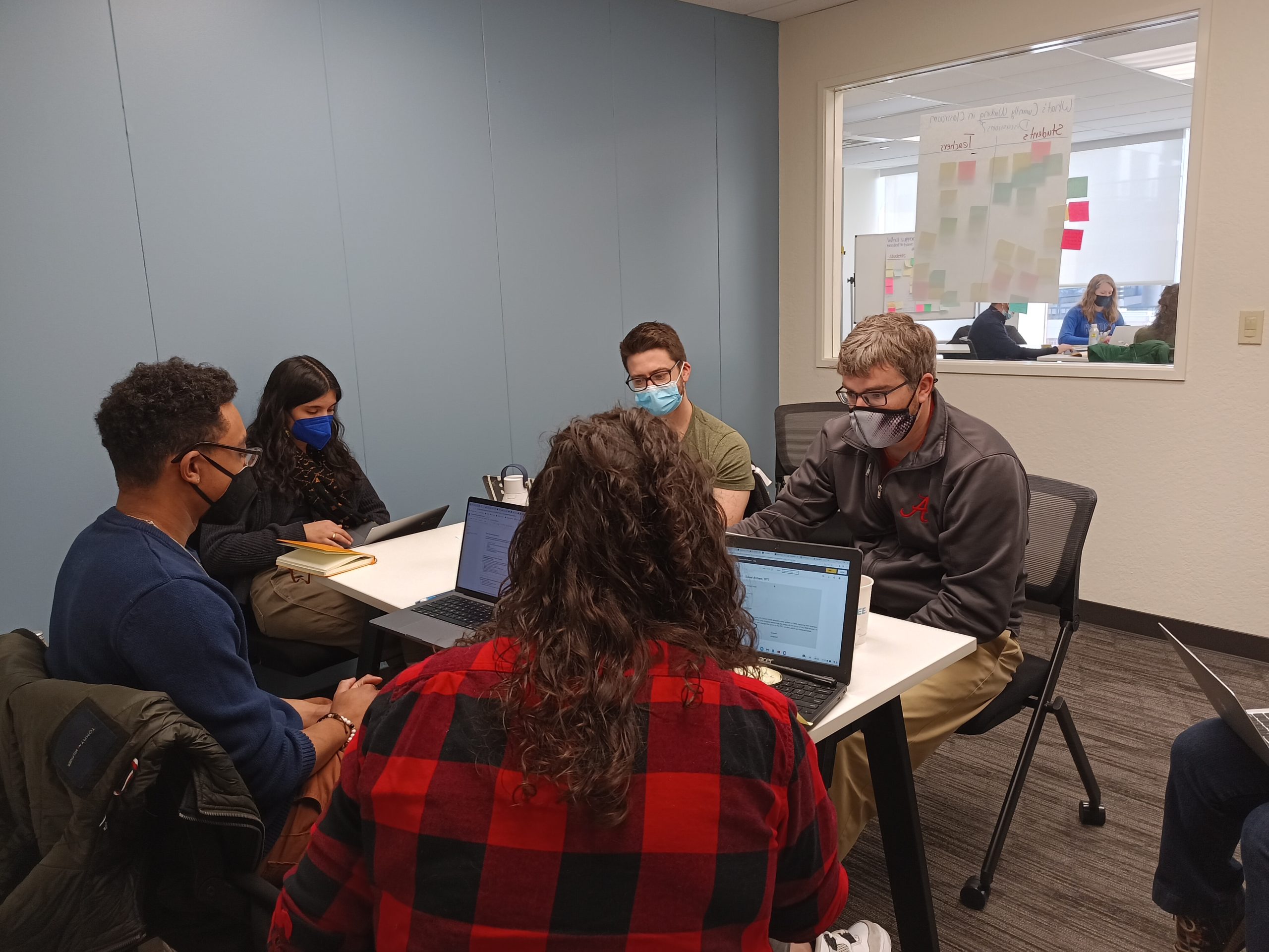 An image of five people sitting around a small table while on their laptops