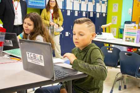 A young white, male student sits at a table and uses a laptop with a sticker on the front that reads TCBOE and underneath, Talladega County Schools #LeadingTheWay