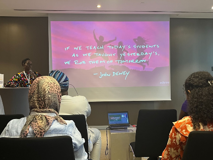 Oluwakemi Olurinola of Olabisi Onabanjo University in Nigeria shares best practices and innovative models for preparing digital teachers. She stands at a podium in front of a presentation slide reading “If we teach today’s students as we taught them yesterday, we rob them of tomorrow.” - John Dewey