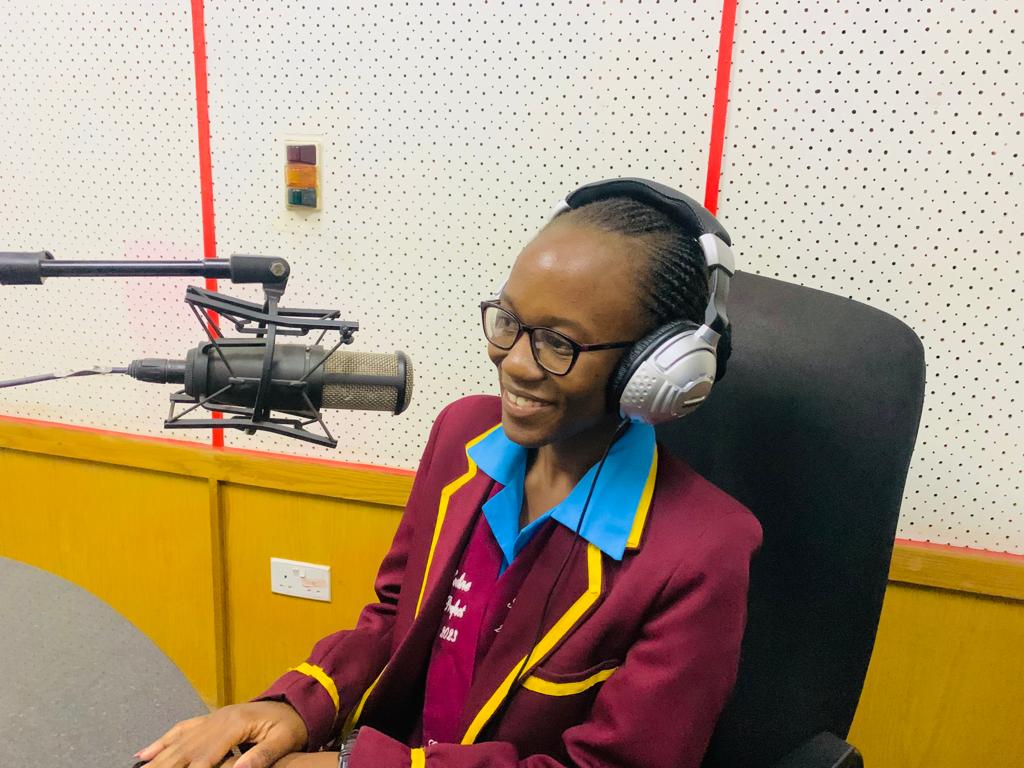 A student has on headphones and sits in front of the microphone at a radio station