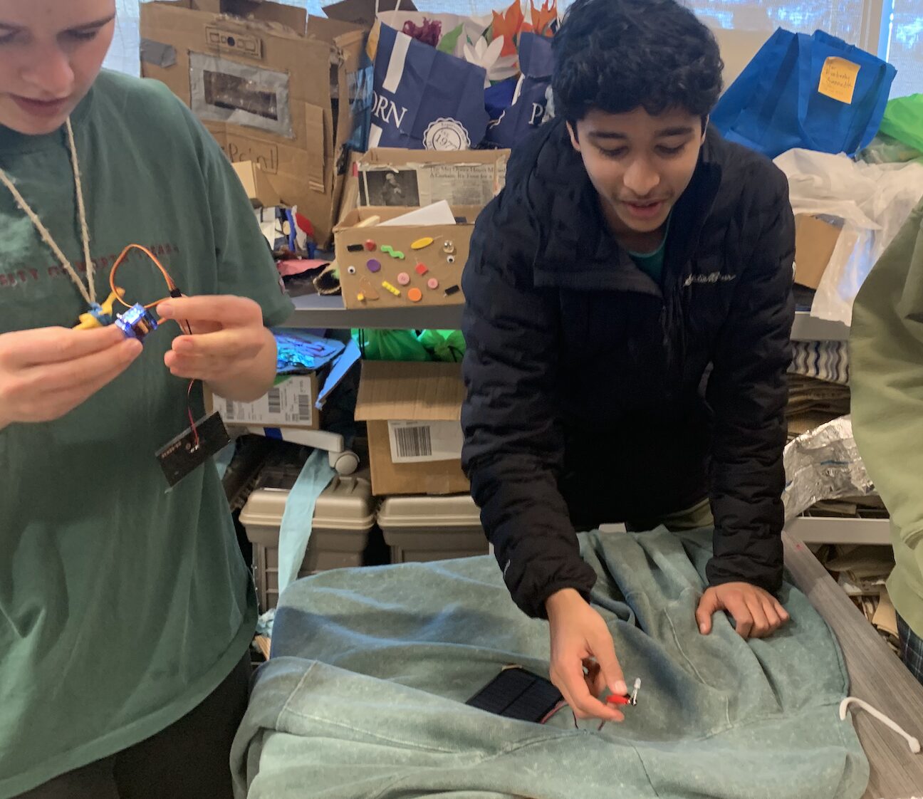 Two students work at a desk with recycled materials. 