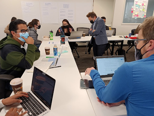 An image of teachers sitting at a u-shaped table with laptops opened in front of them