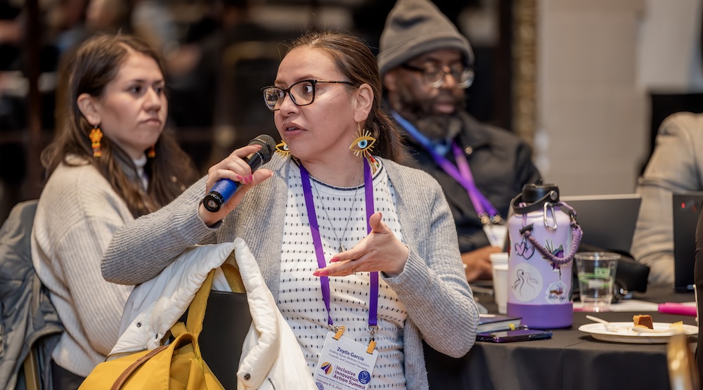 Zeyda Garcia sits in a chair in a plenary session during the Action Summit and speaks into a microphone.